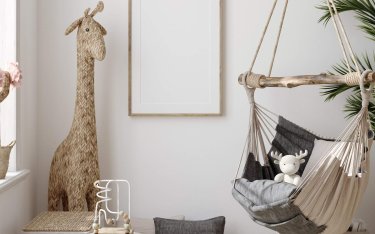 Neutrales Kinderzimmer mit einem Hängesessel, Plüschtieren, einer Korbgiraffe, einem kleinen Aktivitätstisch und gerahmter Kunst an der Wand.